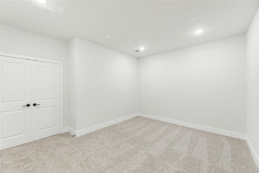 Empty bedroom with white walls, carpet flooring, and double closet doors with black handles