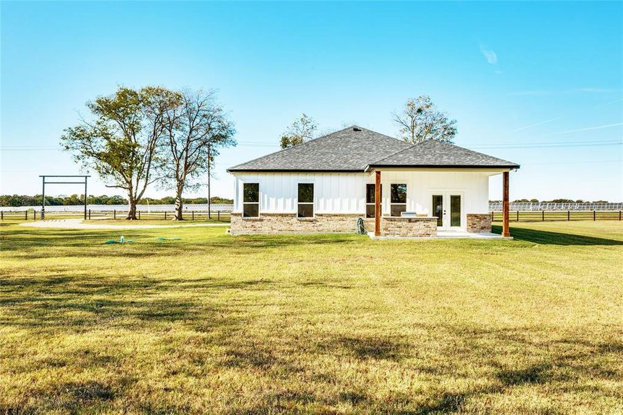 Back of property featuring a patio, roof with shingles, french doors, board and batten siding, and brick siding
