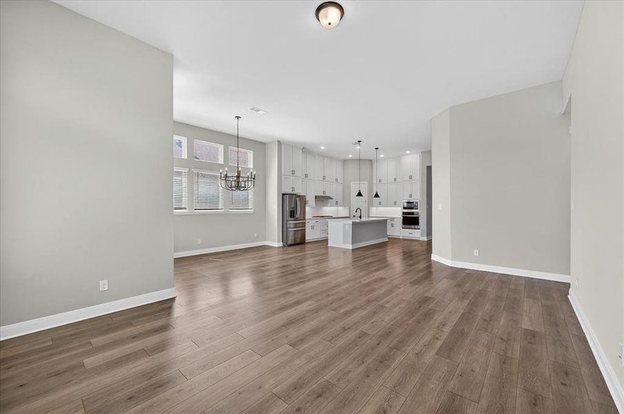 Spacious open-concept interior featuring wood-finish flooring, light gray walls, a contemporary kitchen with a center island, stainless steel appliances, and abundant white cabinetry Spacious open-concept interior featuring wood-finish flooring, light gray walls, a contemporary kitchen with a center island, stainless steel appliances, and abundant white cabinetry