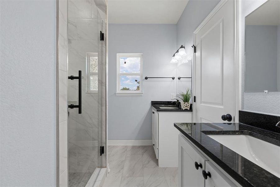 Full bathroom featuring two vanities, a stall shower, and light marble finish floors