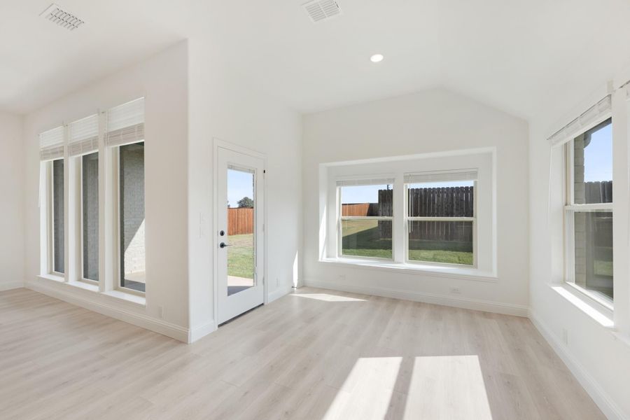 Empty living room with vaulted ceiling, light wood floors, and large windows overlooking backyard