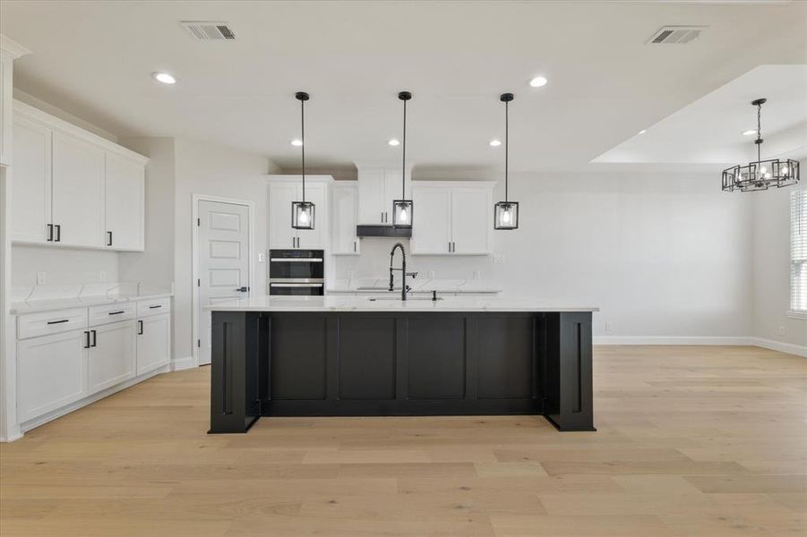 Kitchen with visible vents, a large island with sink, white cabinetry, pendant lighting, and a sink