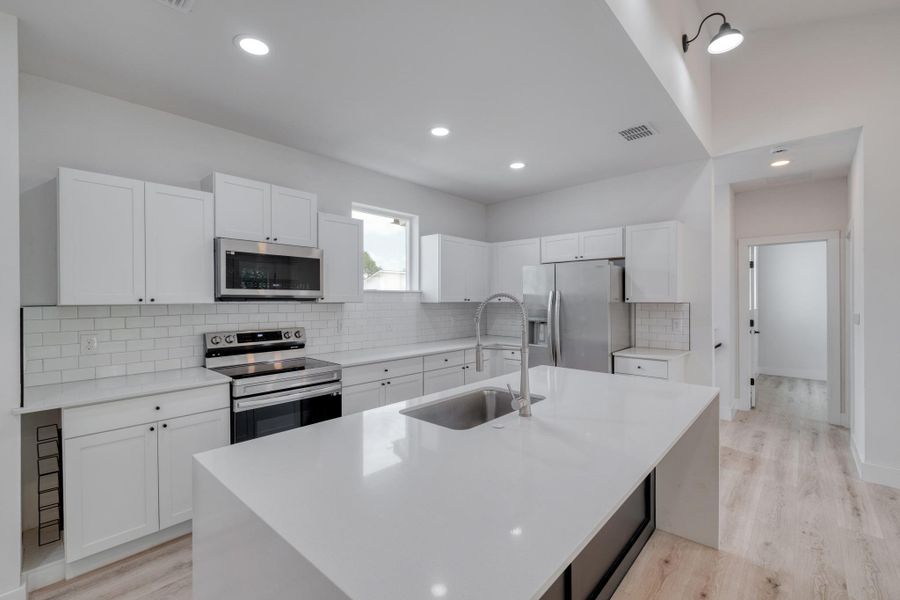 A sleek, contemporary kitchen with white cabinetry, a spacious island, and stainless steel appliances. A sleek, contemporary kitchen with white cabinetry, a spacious island, and stainless steel appliances.