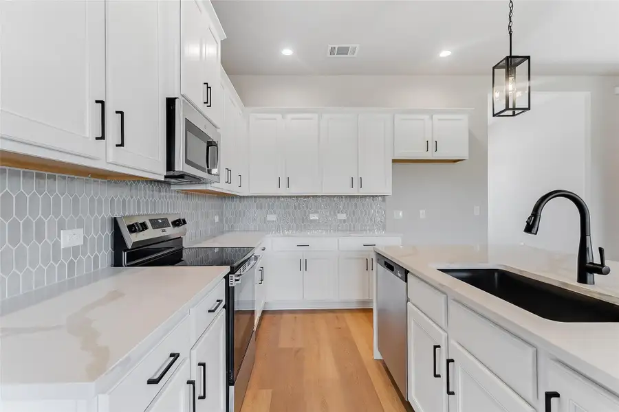 Kitchen with stainless steel appliances, white cabinets, light wood-style floors, and decorative light fixtures