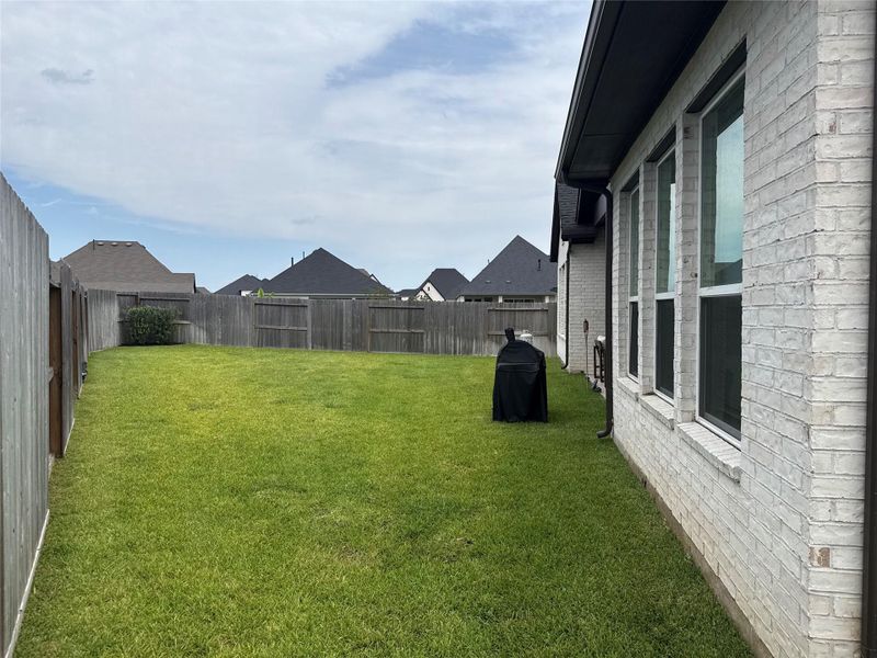 Spacious backyard with well-maintained lawn, privacy fencing, and a side view of the home's brick exterior featuring large windows, perfect for outdoor activities and relaxation.