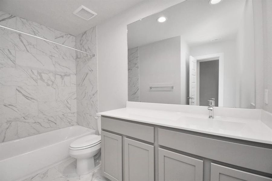 The secondary bath boasts stylish tile flooring, a bath/shower combo with a sleek tile surround, slate colored wood cabinets, and a stunning light countertop. Sample photo of completed home with similar floor plan. As-built interior colors and selections may vary.