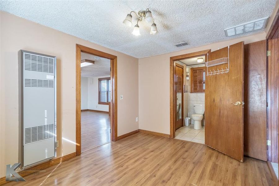 Unfurnished bedroom with a heating unit, light wood-style floors, a textured ceiling, and ensuite bath Unfurnished bedroom with a heating unit, light wood-style floors, a textured ceiling, and ensuite bath