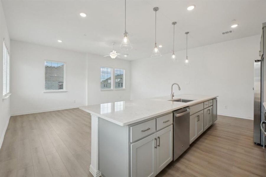 Kitchen featuring gray cabinetry, a kitchen island with sink, hanging light fixtures, stainless steel dishwasher, and ceiling fan