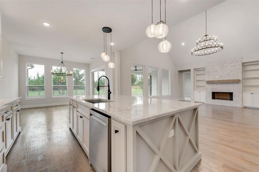 Kitchen with dishwasher, a center island with sink, a stone fireplace, white cabinetry, and light wood-type flooring