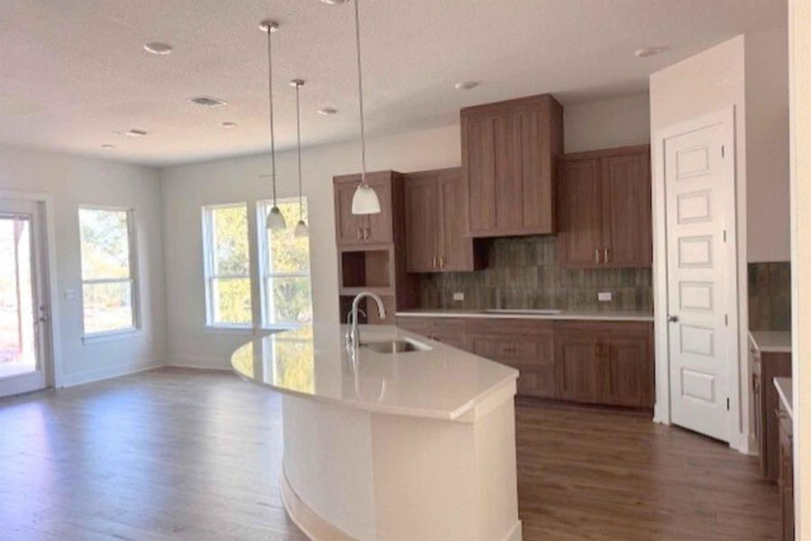 Kitchen with dark wood-style flooring, wood finish cabinetry, a center island with sink, decorative light fixtures, and cooktop