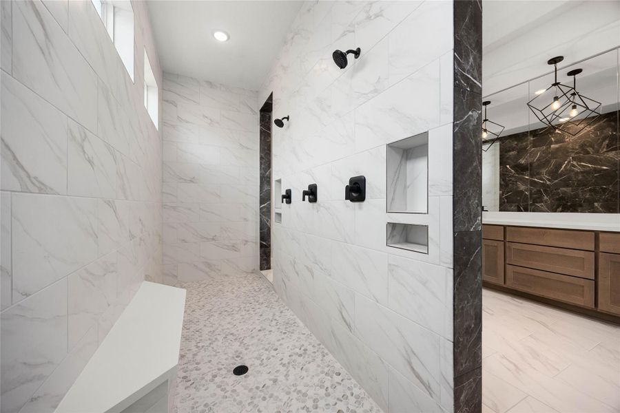 Carwash-style walk-in shower delivering a true resort-level experience. This massive open-concept wet room features stunning floor-to-ceiling white marble-look wall tile, an elegant pebble-stone floor tile layout, and a long built-in bench seat. Equipped with dual matte black shower heads and control valves, high transom windows for natural light, and integrated storage niches, this custom setup combines ultimate utility with modern design. Carwash-style walk-in shower delivering a true resort-level experience. This massive open-concept wet room features stunning floor-to-ceiling white marble-look wall tile, an elegant pebble-stone floor tile layout, and a long built-in bench seat. Equipped with dual matte black shower heads and control valves, high transom windows for natural light, and integrated storage niches, this custom setup combines ultimate utility with modern design.