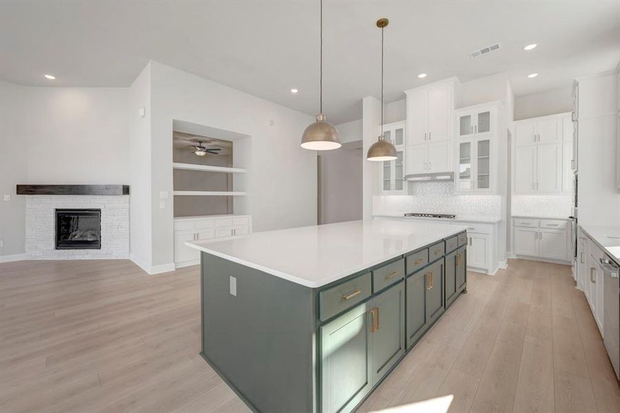 Kitchen featuring two tone cabinetry, light wood-style flooring, decorative light fixtures, decorative backsplash, and a center island