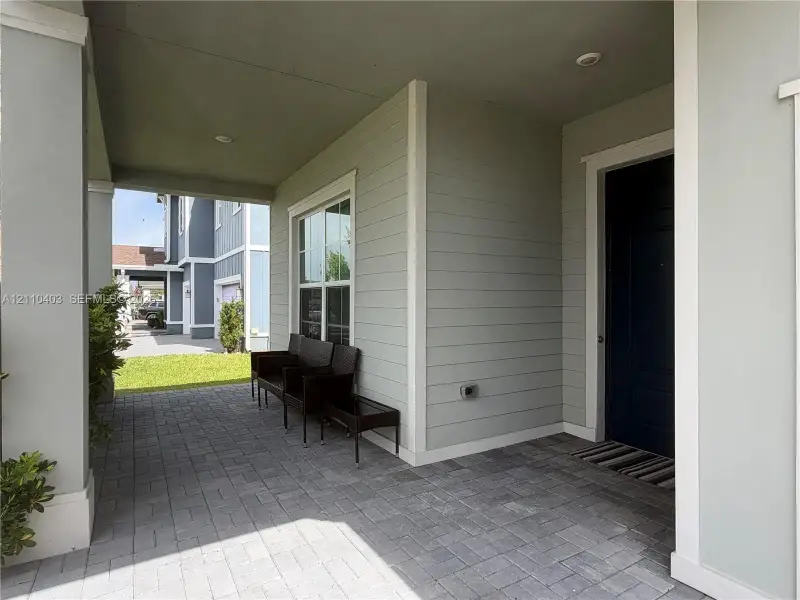 Covered front entry featuring light green lap siding, paver flooring, recessed lighting, and a solid-panel door with white trim