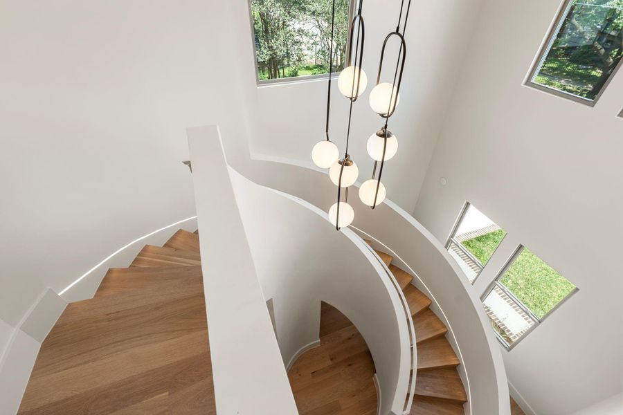 Transitioning upstairs, the sleek sculptural staircase winds to the second floor, framed by dramatic 20-foot ceilings that enhance the home’s scale as multiple windows flood the foyer and second-floor landing with natural light. Transitioning upstairs, the sleek sculptural staircase winds to the second floor, framed by dramatic 20-foot ceilings that enhance the home’s scale as multiple windows flood the foyer and second-floor landing with natural light.