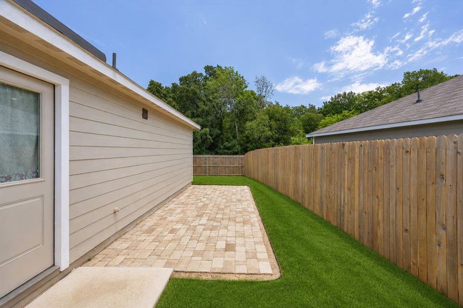 Outdoor living space featuring a textured paver patio, artificial turf, and a wood privacy fence