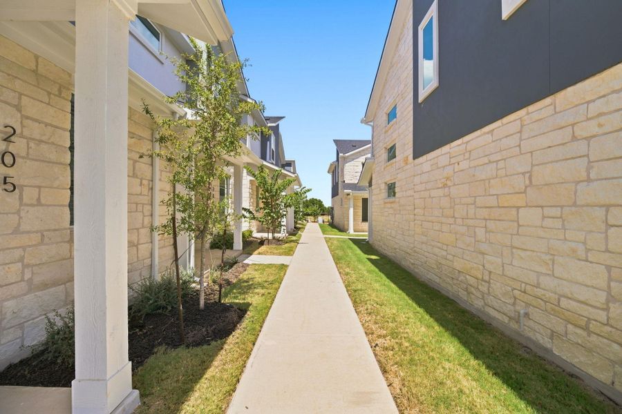 A paved concrete walkway guides the way between modern stone-accented homes under a clear blue sky.