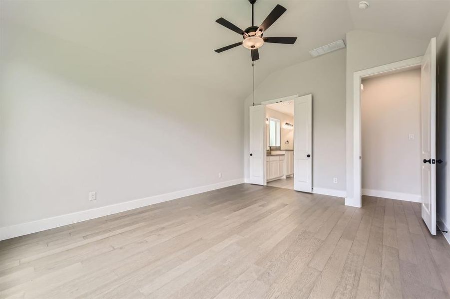 Unfurnished bedroom featuring lofted ceiling, light wood-style flooring, baseboards, ensuite bath, and a ceiling fan