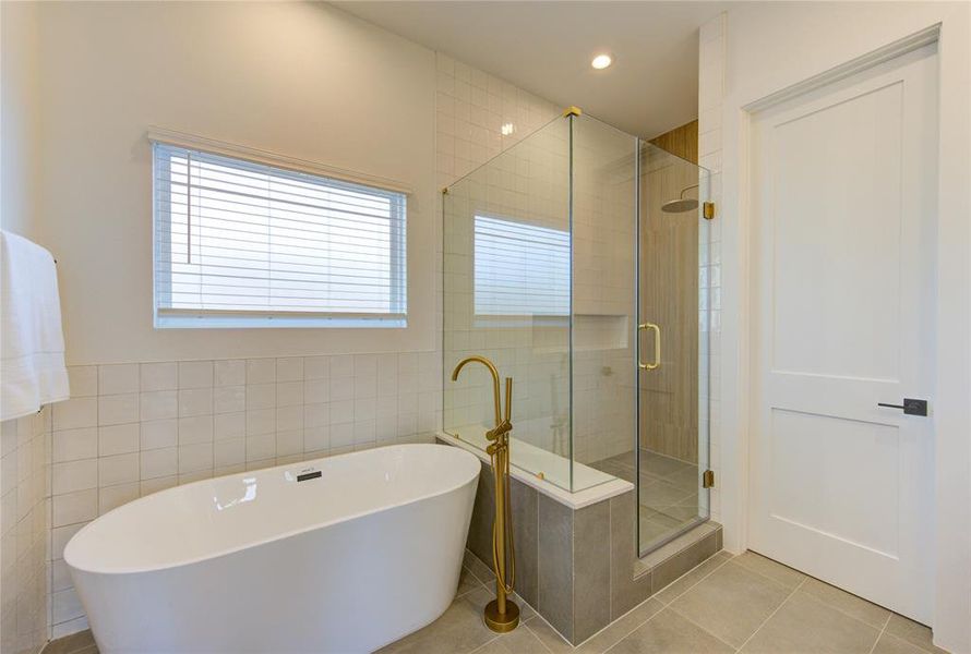 This primary bathroom feels like a spa with designer tile work, elegant champagne bronze fixtures, large soaking tub and walk-in shower, double vanity, and separated toilet room.