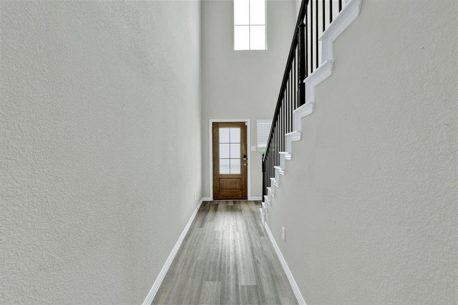 Welcoming entryway featuring a wooden door with glass panels, light-colored walls, and durable flooring, alongside a staircase with black railings