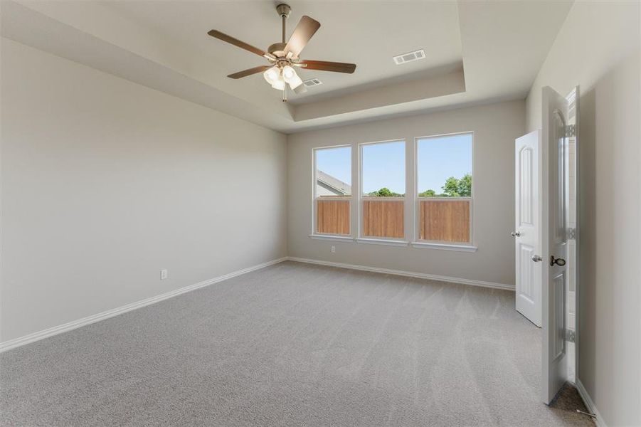 Empty room featuring light colored carpet, a ceiling fan, and a tray ceiling