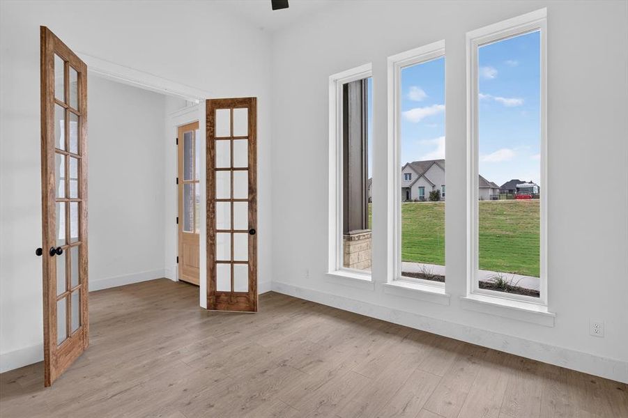 Room featuring three tall windows, light wood-finish flooring, white baseboards, and double French doors with black hardware Room featuring three tall windows, light wood-finish flooring, white baseboards, and double French doors with black hardware