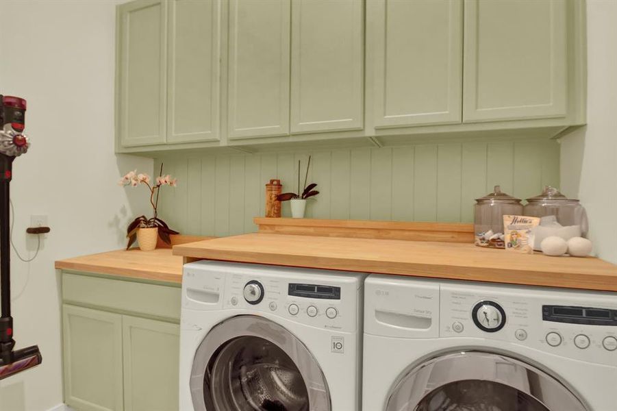 A tidy laundry room featuring a custom space for a front-loading washer and dryer with a wooden countertop and sage green cabinetry for ample storage.