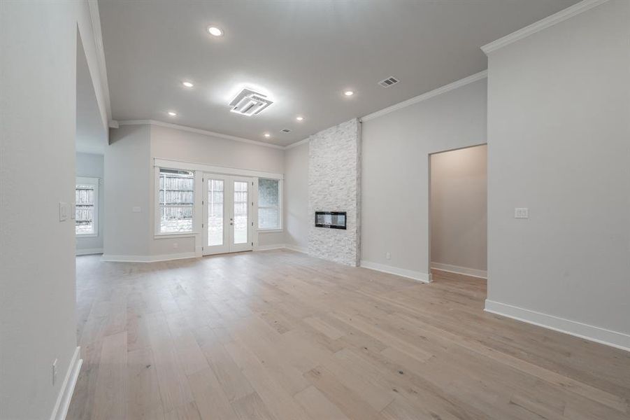 Unfurnished living room with french doors, ornamental molding, light wood finished floors, recessed lighting, and a fireplace