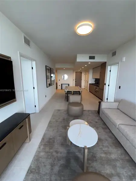 Open-concept interior featuring light-toned flooring, recessed ceiling lighting, flush-mount lighting, and custom cabinetry with integrated kitchen appliances Open-concept interior featuring light-toned flooring, recessed ceiling lighting, flush-mount lighting, and custom cabinetry with integrated kitchen appliances