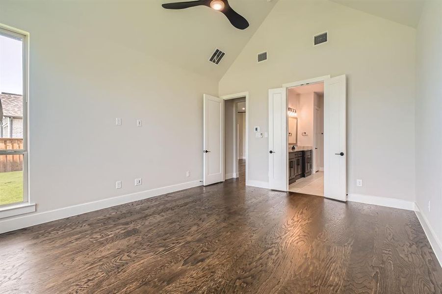 Unfurnished bedroom featuring wood finished floors, high vaulted ceiling, connected bathroom, and a ceiling fan Unfurnished bedroom featuring wood finished floors, high vaulted ceiling, connected bathroom, and a ceiling fan