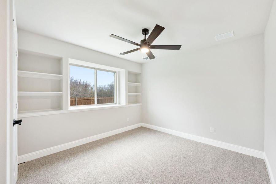 Empty bedroom with built-in shelves, ceiling fan, carpet flooring, and a window with backyard view