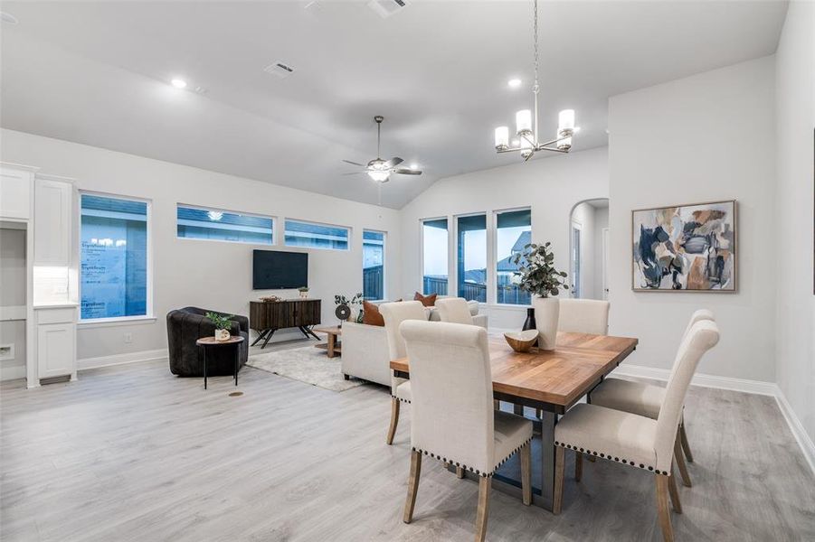 Dining room with ceiling fan with notable chandelier, light hardwood / wood-style floors, and vaulted ceiling