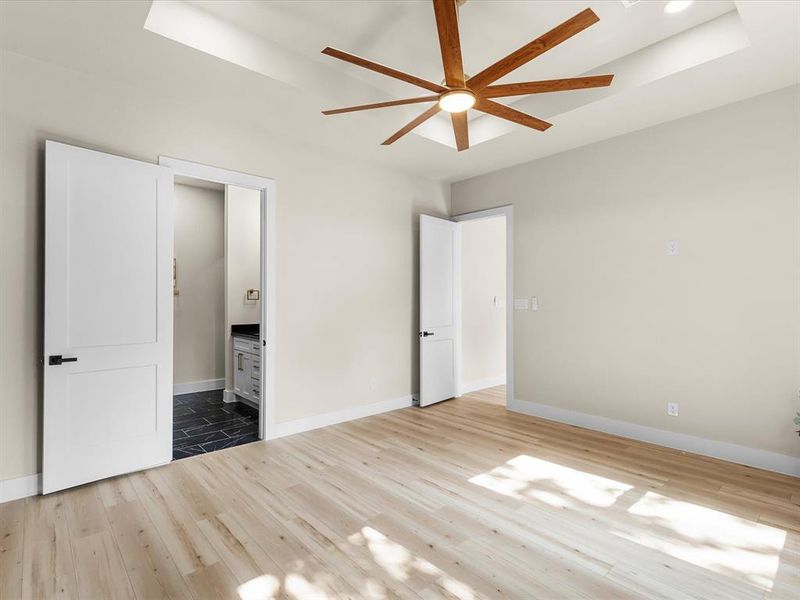 Spacious room featuring wood-finish flooring and a tray ceiling with a modern ceiling fan