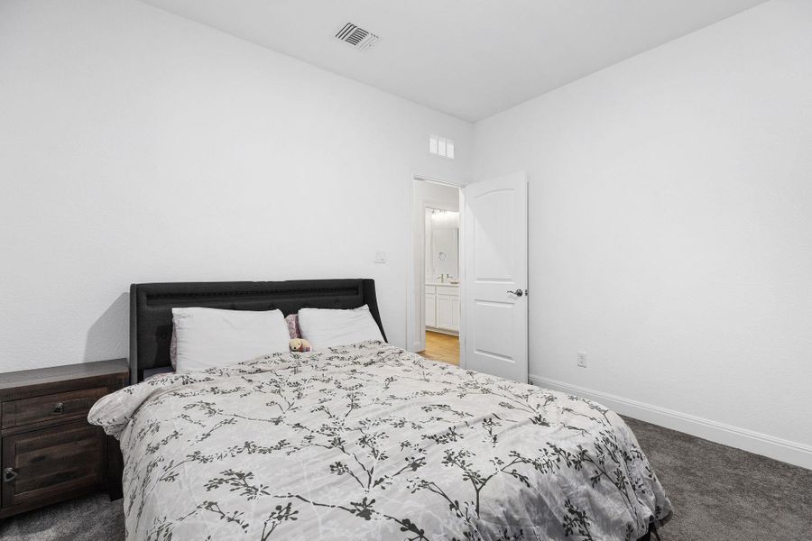 A well-lit bedroom features plush carpeting and convenient access to a private bathroom.