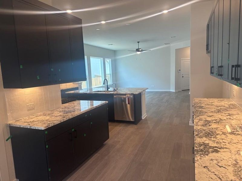 Kitchen with tasteful backsplash, dark cabinetry, dark wood-type flooring, and light stone countertops Kitchen with tasteful backsplash, dark cabinetry, dark wood-type flooring, and light stone countertops