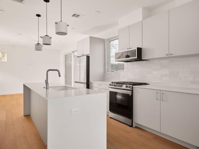 Kitchen featuring stainless steel range with gas cooktop, pendant lighting, a center island with sink, freestanding refrigerator, and decorative backsplash