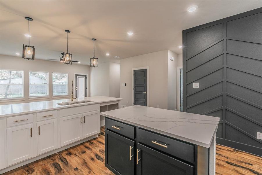 Kitchen with light stone countertops, light wood-type flooring, white cabinets, a kitchen island, and hanging light fixtures