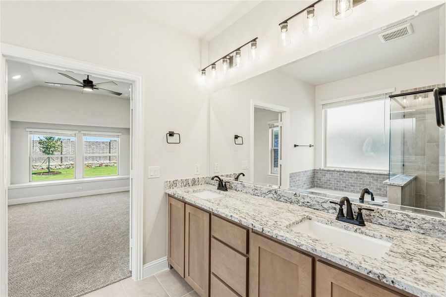 Master bathroom with double granite vanity, glass shower, and view into carpeted bedroom with vaulted ceiling
