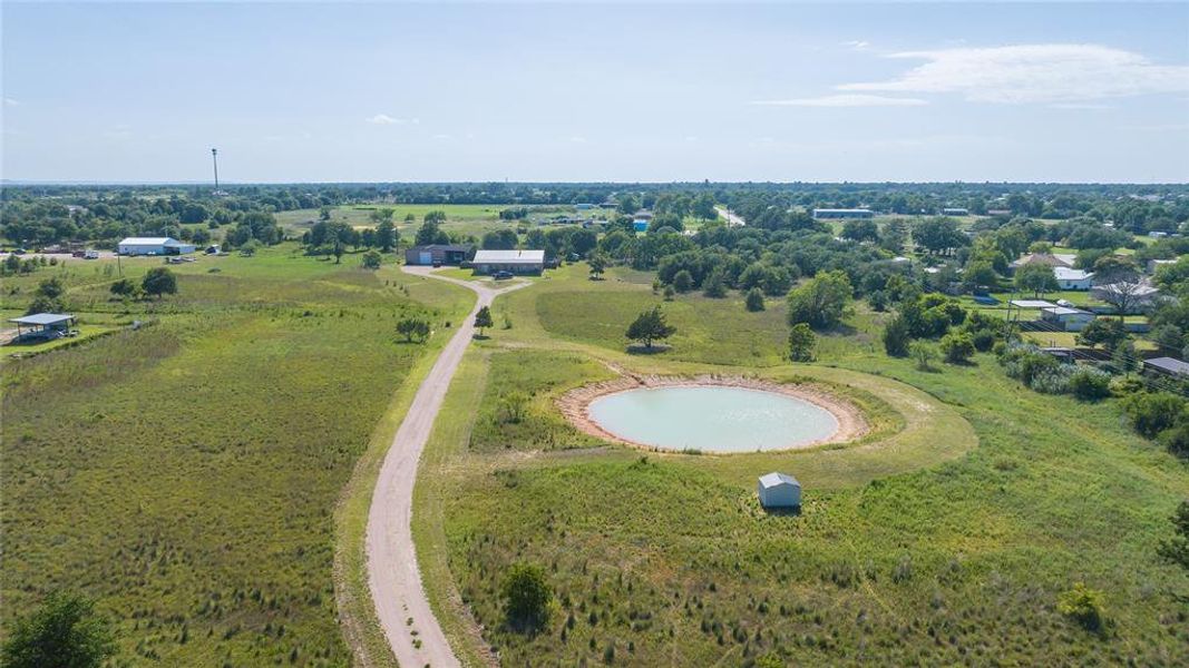 Expansive property featuring a central pond, gravel driveway, multiple outbuildings, and mature trees Expansive property featuring a central pond, gravel driveway, multiple outbuildings, and mature trees