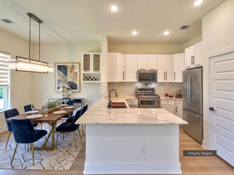 Open-concept kitchen and dining area featuring light wood-finish flooring, white cabinetry, stainless steel appliances, a white island with veining, and a complementary white backsplash with veining