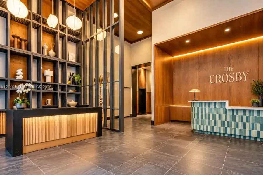 Double-height lobby featuring floor-to-ceiling grid shelving, integrated wood-paneled walls, tile-accented reception desk, and stone-finish flooring Double-height lobby featuring floor-to-ceiling grid shelving, integrated wood-paneled walls, tile-accented reception desk, and stone-finish flooring