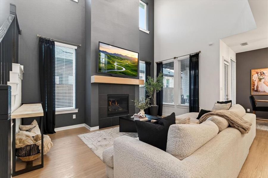 Living room featuring healthy amount of natural light, a tiled fireplace, light wood-style floors, and a high ceiling Living room featuring healthy amount of natural light, a tiled fireplace, light wood-style floors, and a high ceiling