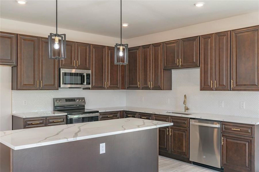 Kitchen featuring sink, stainless steel appliances, hanging light fixtures, and light stone countertops