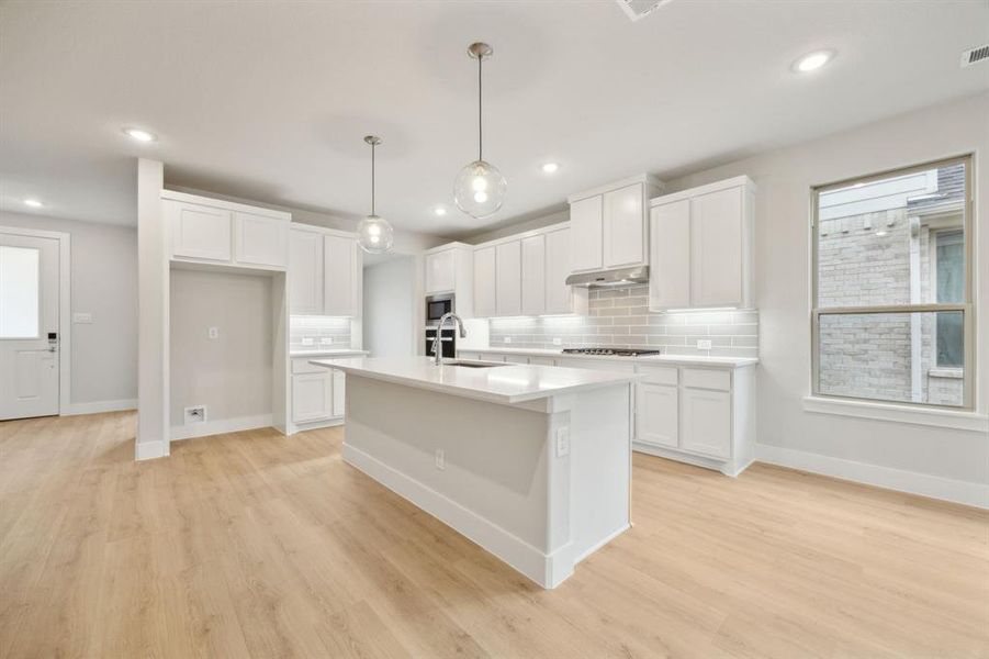 Kitchen with pendant lighting, appliances with stainless steel finishes, white cabinetry, a kitchen island with sink, and light wood-type flooring