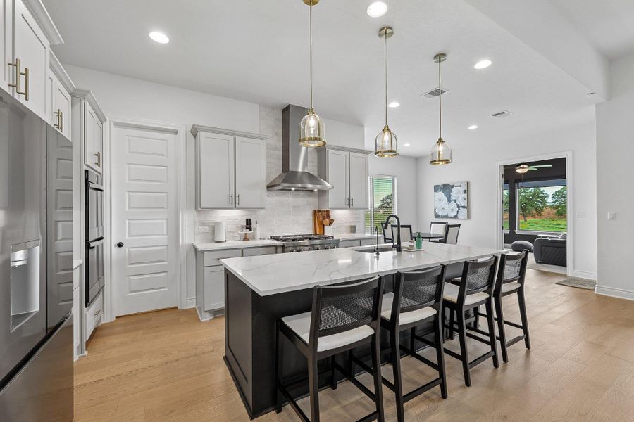 Gourmet kitchen featuring a large central island with seating, stainless steel appliances, light wood-finish flooring, recessed lighting, and pendant fixtures