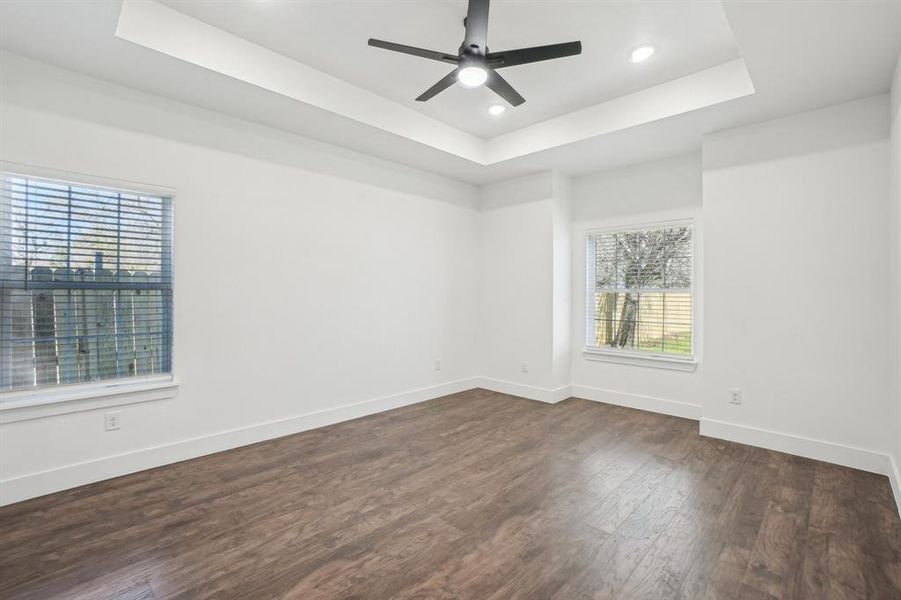 Primary bedroom with dark hardwood / wood-style flooring, a tray ceiling, plenty of natural light, and ceiling fan