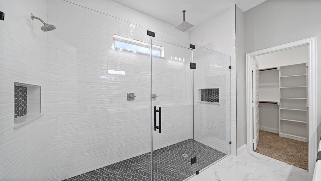 Bathroom featuring marble finish floor, a stall shower, a walk in closet, and baseboards