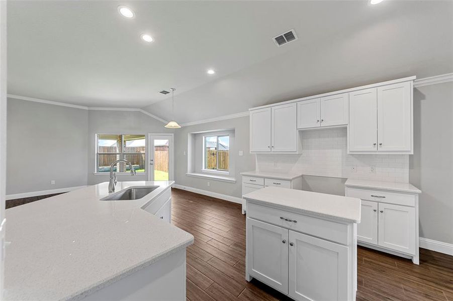 Kitchen featuring dark wood-type flooring, sink, white cabinets, lofted ceiling, and an island with sink