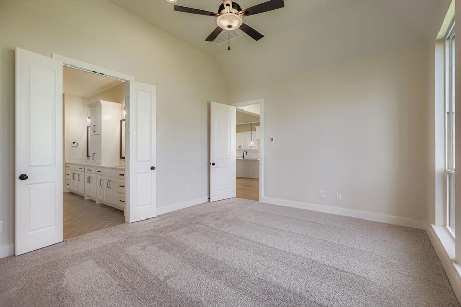 Unfurnished bedroom featuring light colored carpet, vaulted ceiling, a ceiling fan, and ensuite bath
