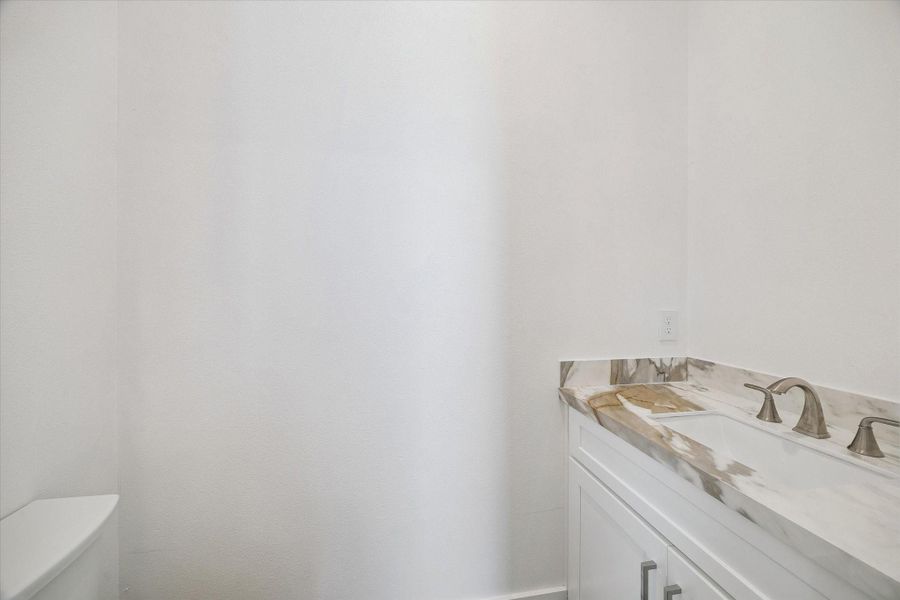 A convenient powder room carries the home’s clean contemporary finishes into a compact, functional space. The white vanity is topped with a striking stone-look counter and backsplash, complemented by a brushed-metal faucet and simple modern hardware. Crisp white walls keep the room light and versatile, while the streamlined design feels fresh and polished. Thoughtful finishes echo the style found throughout the home, giving even this practical guest space a cohesive, elevated appearance. A convenient powder room carries the home’s clean contemporary finishes into a compact, functional space. The white vanity is topped with a striking stone-look counter and backsplash, complemented by a brushed-metal faucet and simple modern hardware. Crisp white walls keep the room light and versatile, while the streamlined design feels fresh and polished. Thoughtful finishes echo the style found throughout the home, giving even this practical guest space a cohesive, elevated appearance.