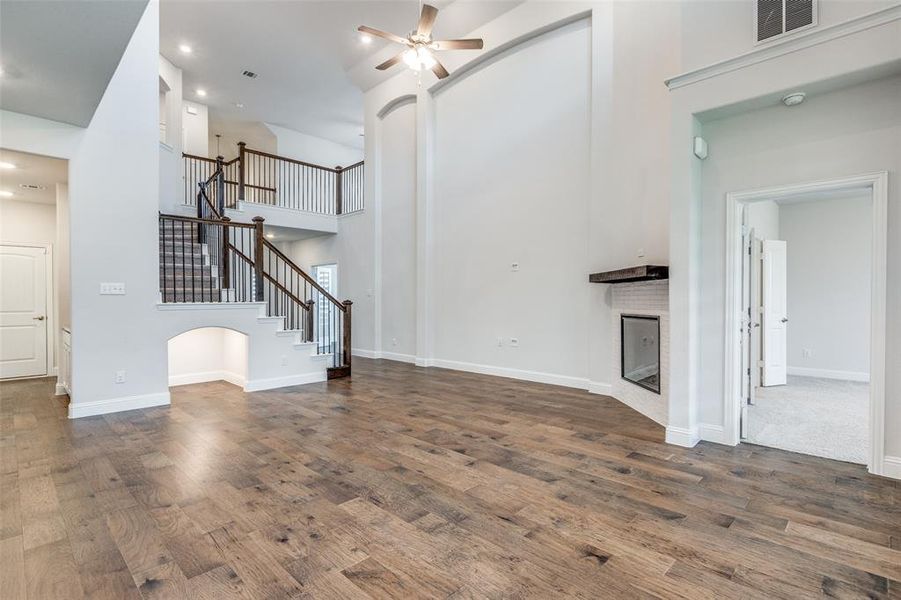 Unfurnished living room with a ceiling fan, a fireplace, a towering ceiling, stairway, and wood finished floors